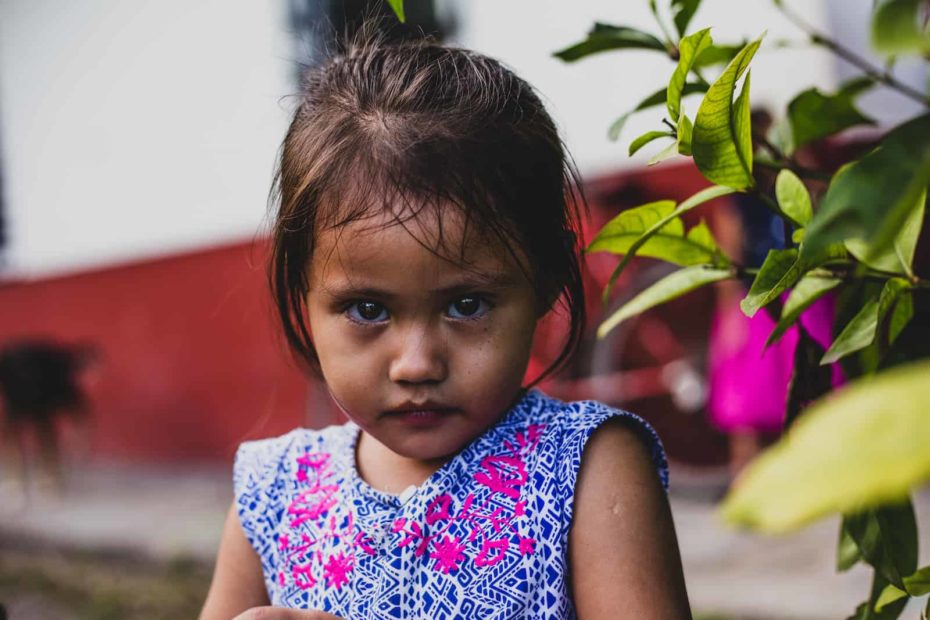 A girl wearing a blue dress looks at the camera with a serious look on her face.