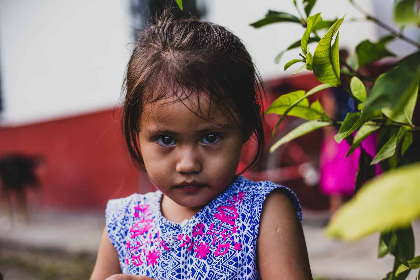 How to Help Kids in Need: A girl wearing a blue dress looks at the camera with a serious look on her face.