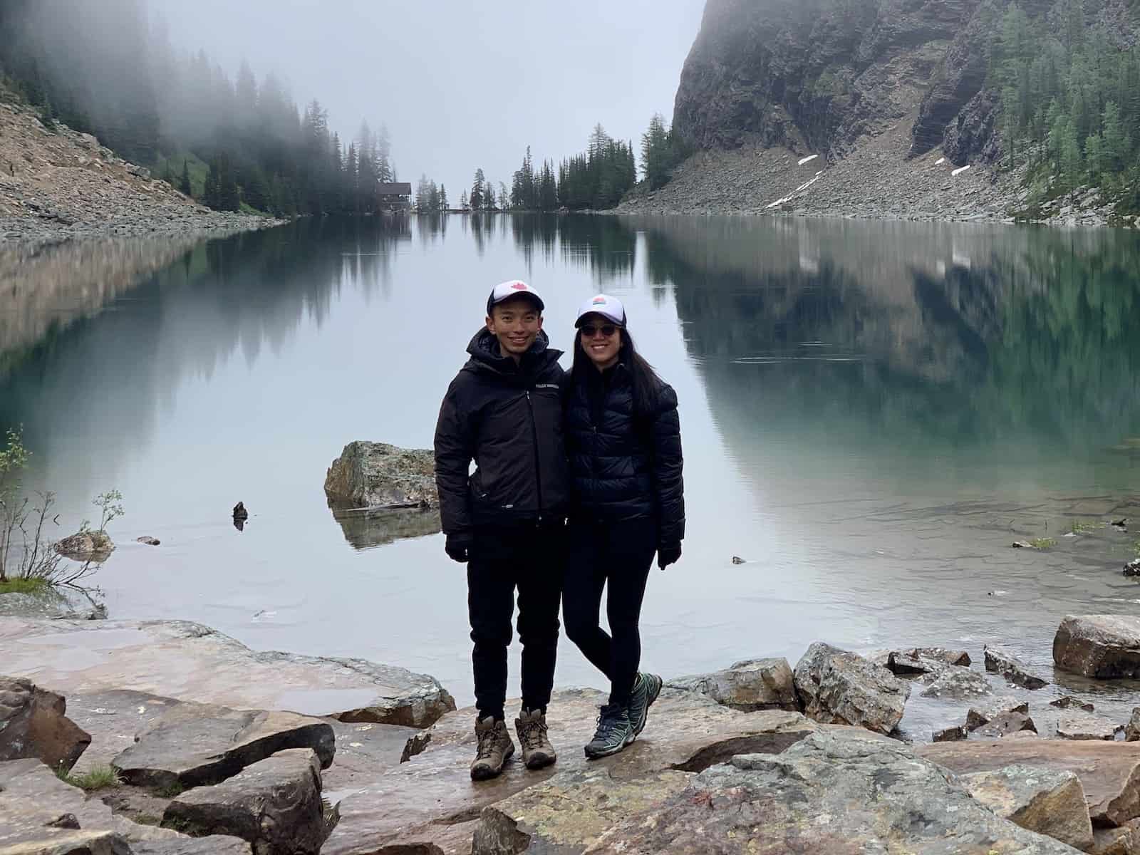 A man and woman stand in front of a mountain lake