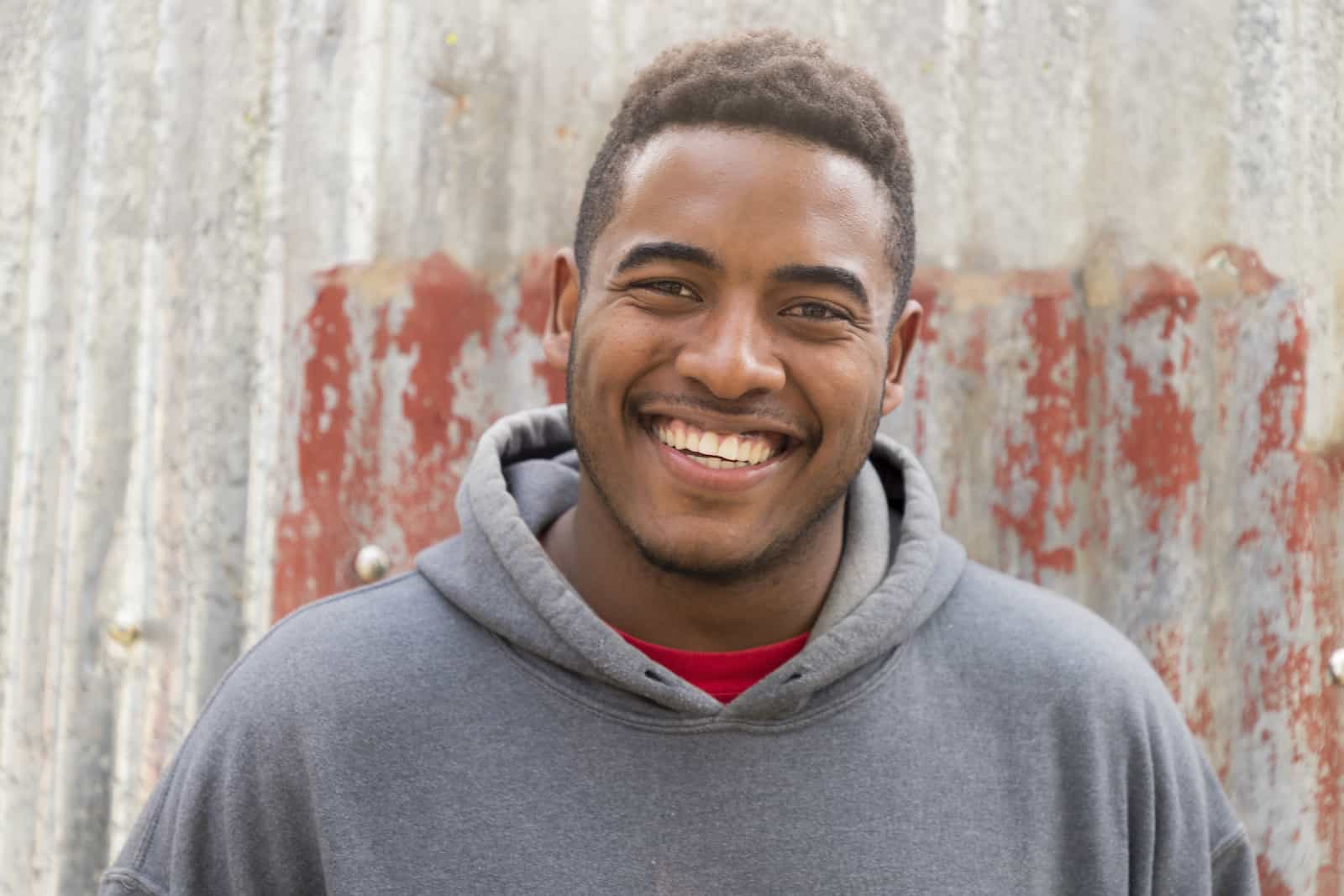 A man in a grey hooded sweatshirt smiles at the camera.