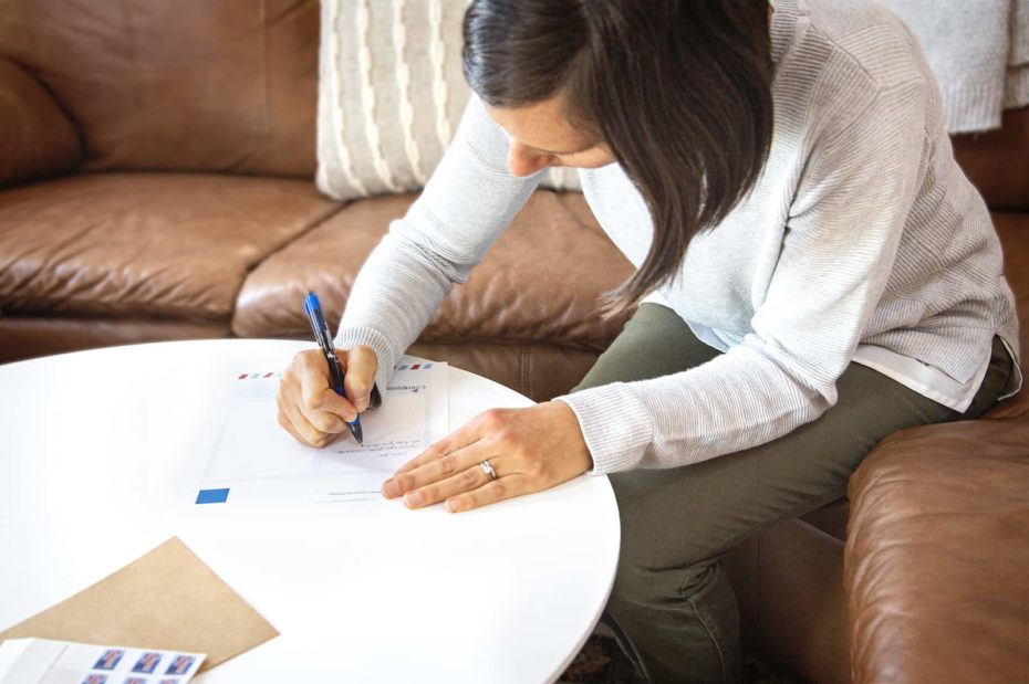 A woman sits at a table, writing a letter.