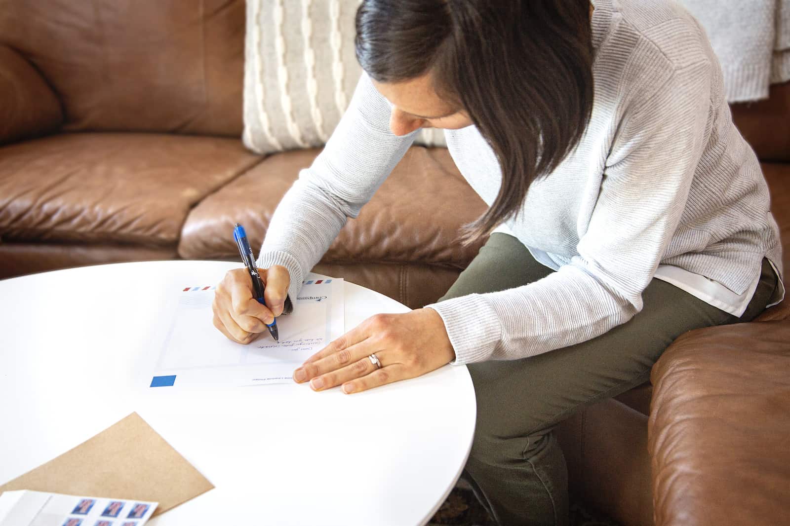 A woman sits at a table, writing a letter. 