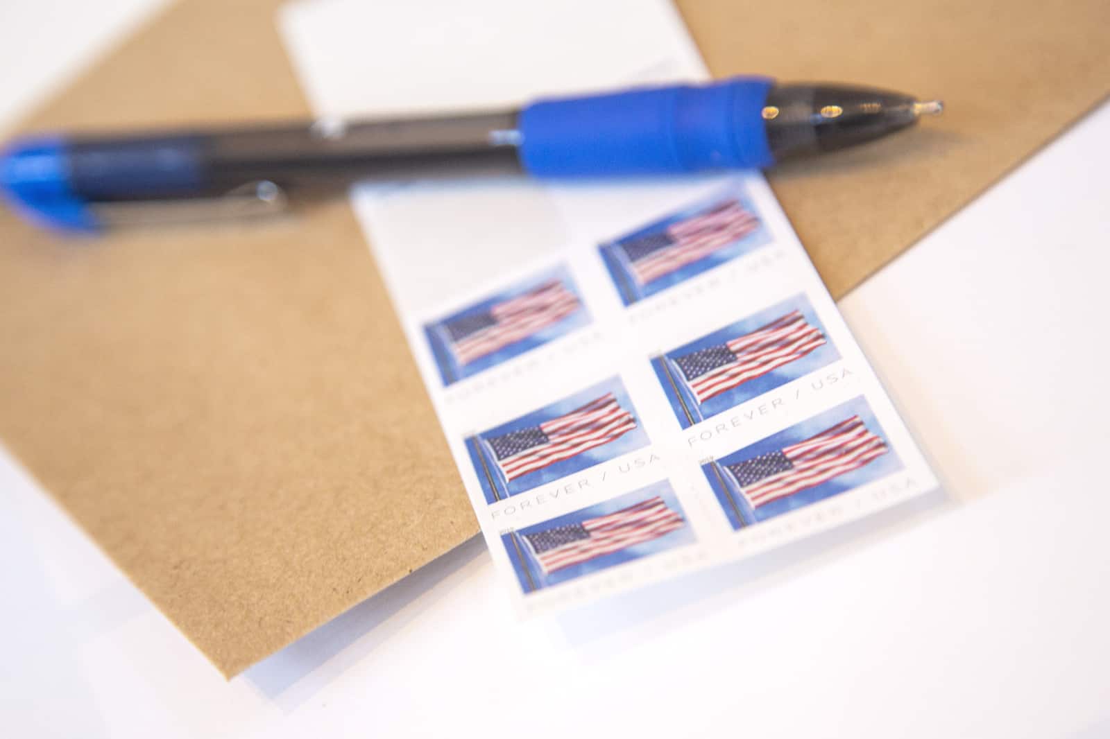 A pen sits atop postage stamps and an envelope.