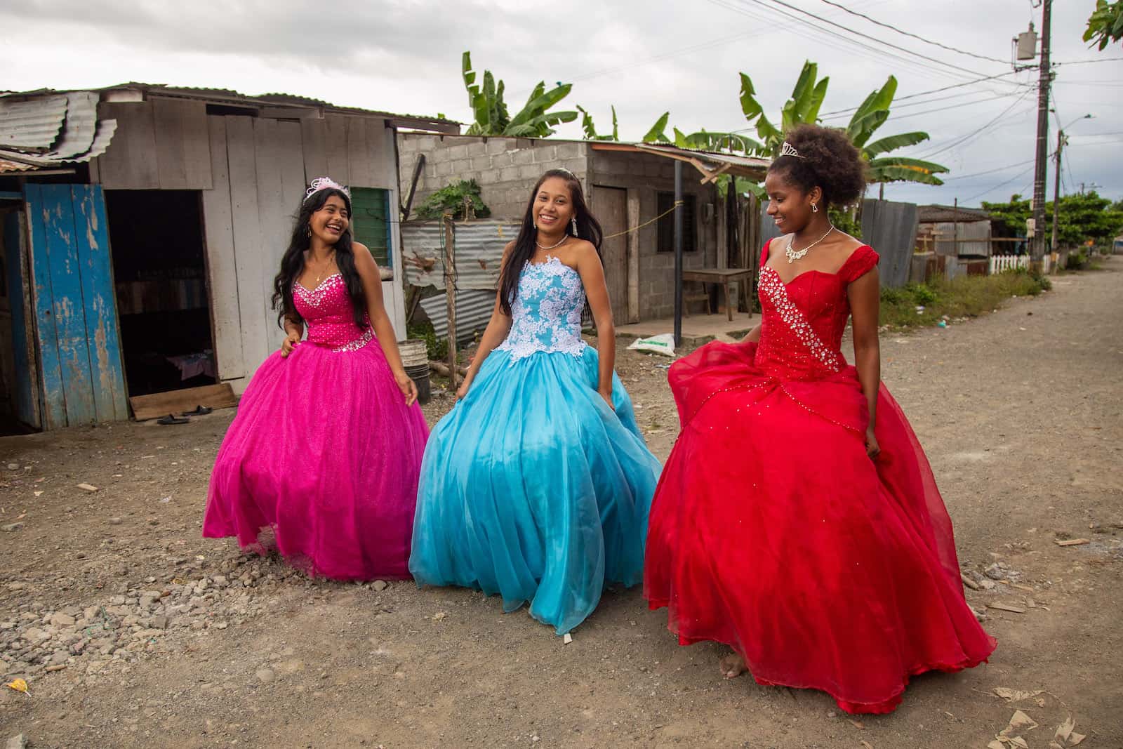 Three girls in formal wear walk down a dirt road. 