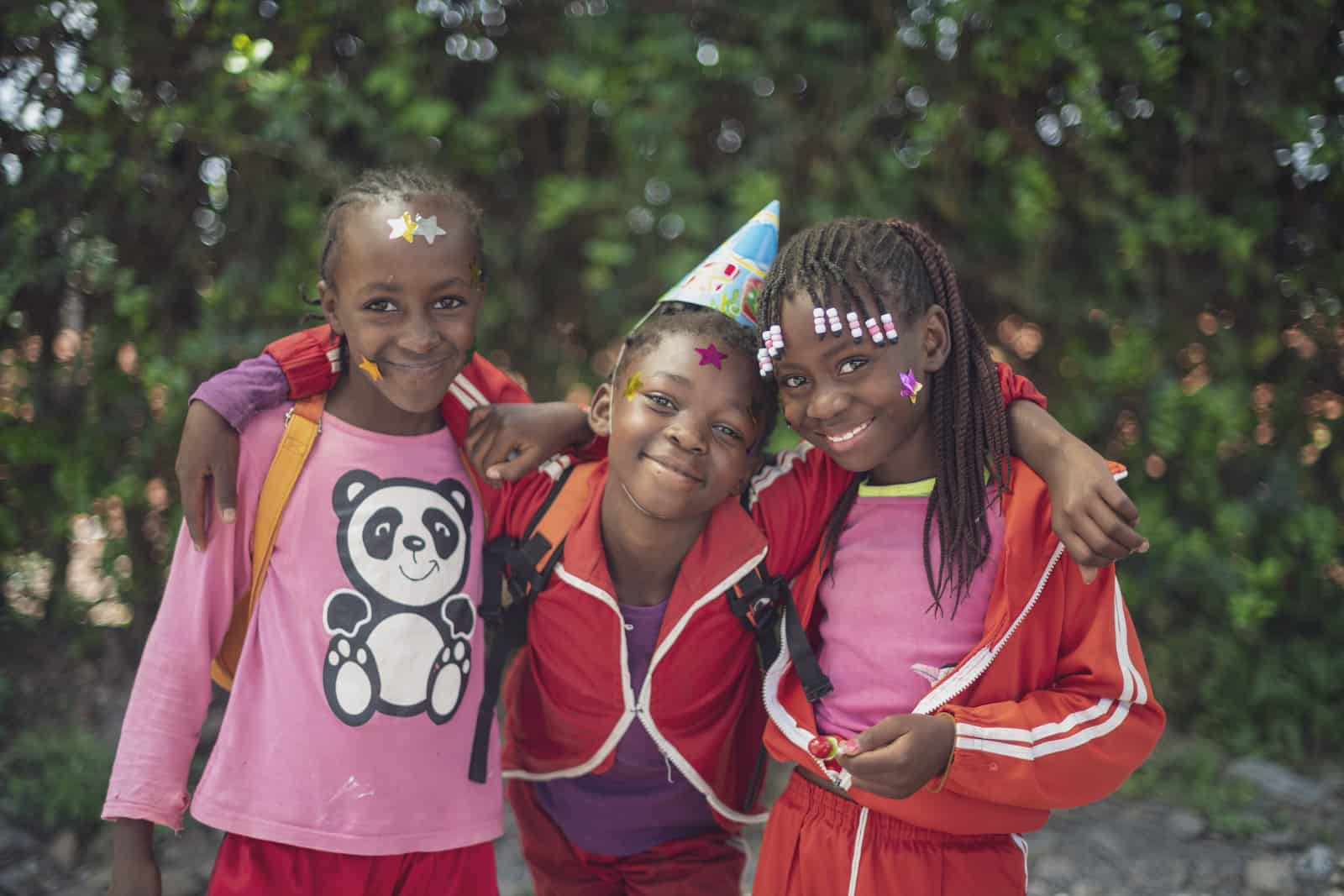 Three girls hug, the center one wearing a party hat. 