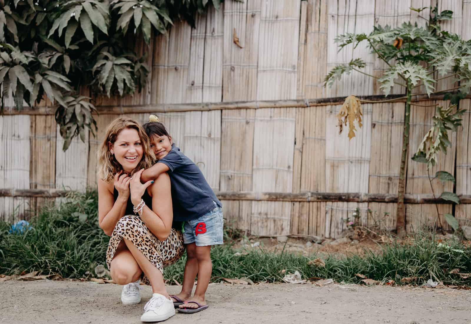 Candace Cameron Bure squats on the ground, with a young girl hugging her. 