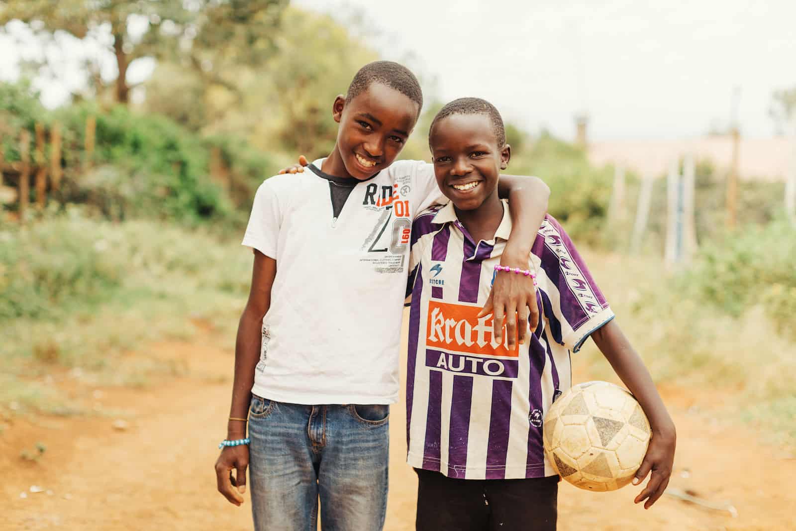 Two boys smile, one holding a soccer ball.