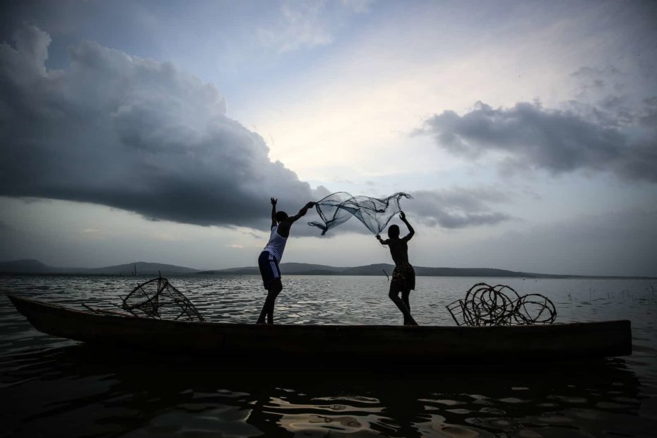 The silhouette of two people throwing a fishing net into a lake.