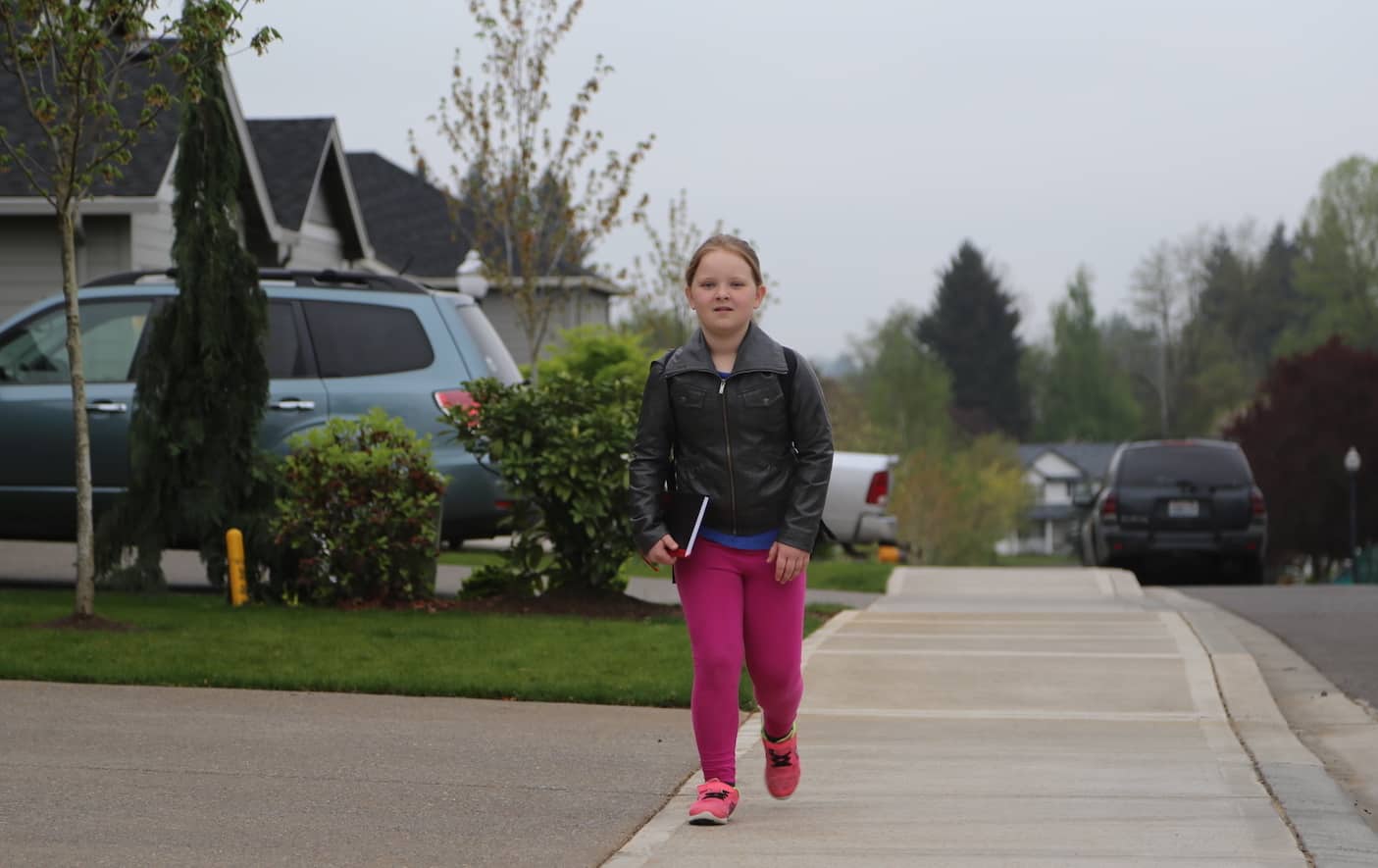 A girl walks down a street block, carrying a backpack.