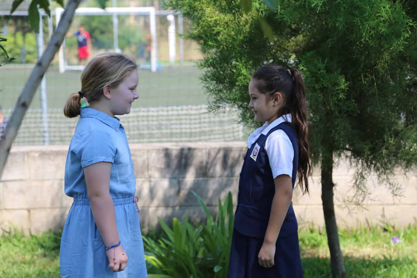 Two girls stand on a field, looking at each other.