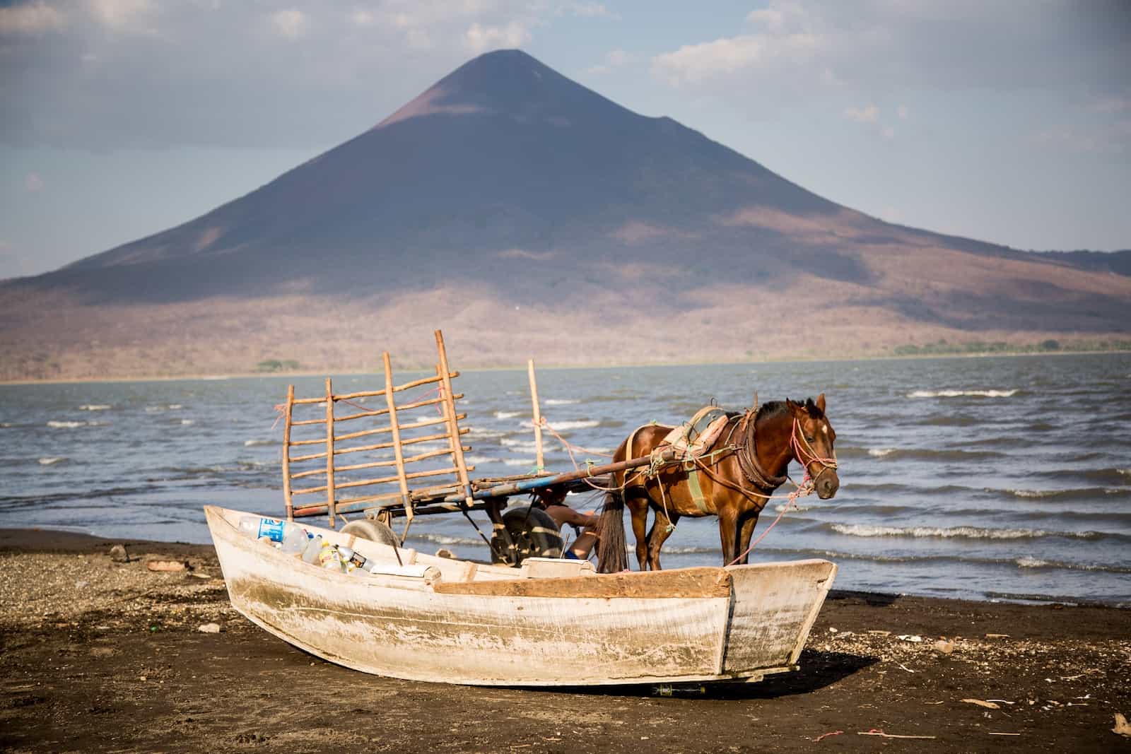 A horse stands next to a boat in front of a lake and volcano where tourism is down after Nicaragua unrest.