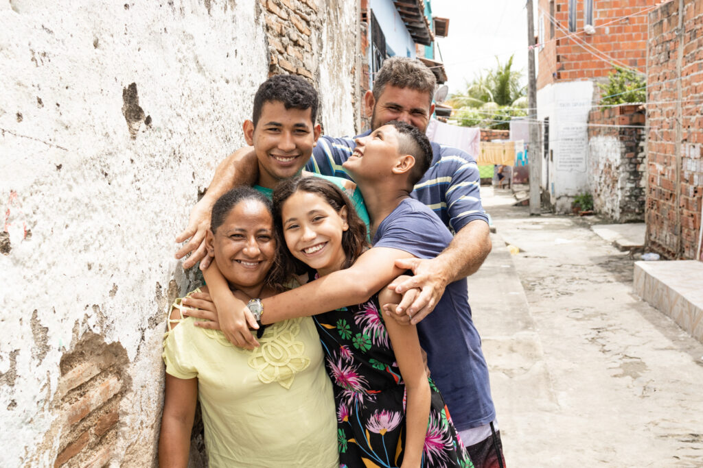 A family of five hugs each other while leaning against a stone wall. They smile for the camera.