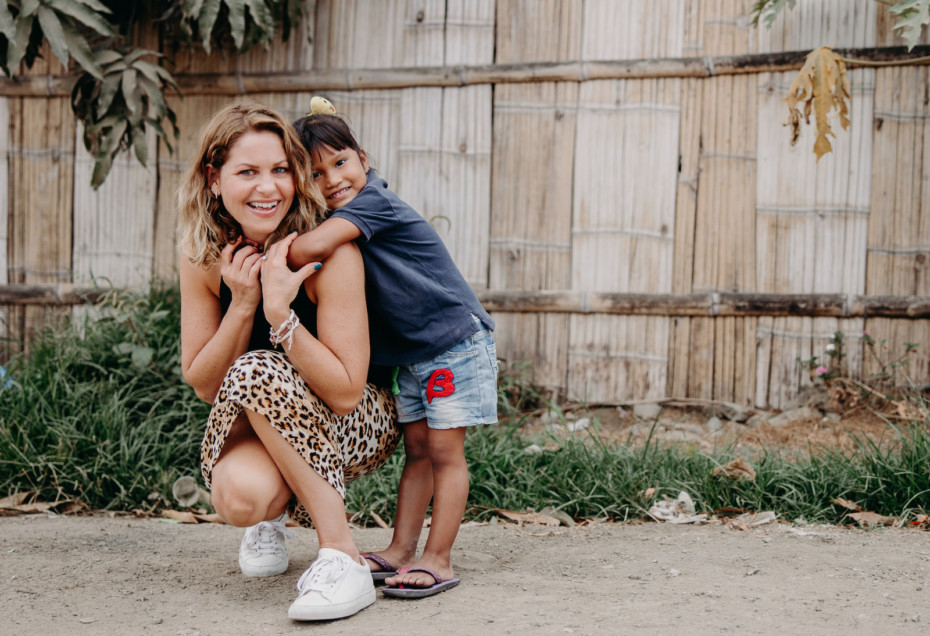 Candace Cameron Bure squats on the ground, with a young girl hugging her.