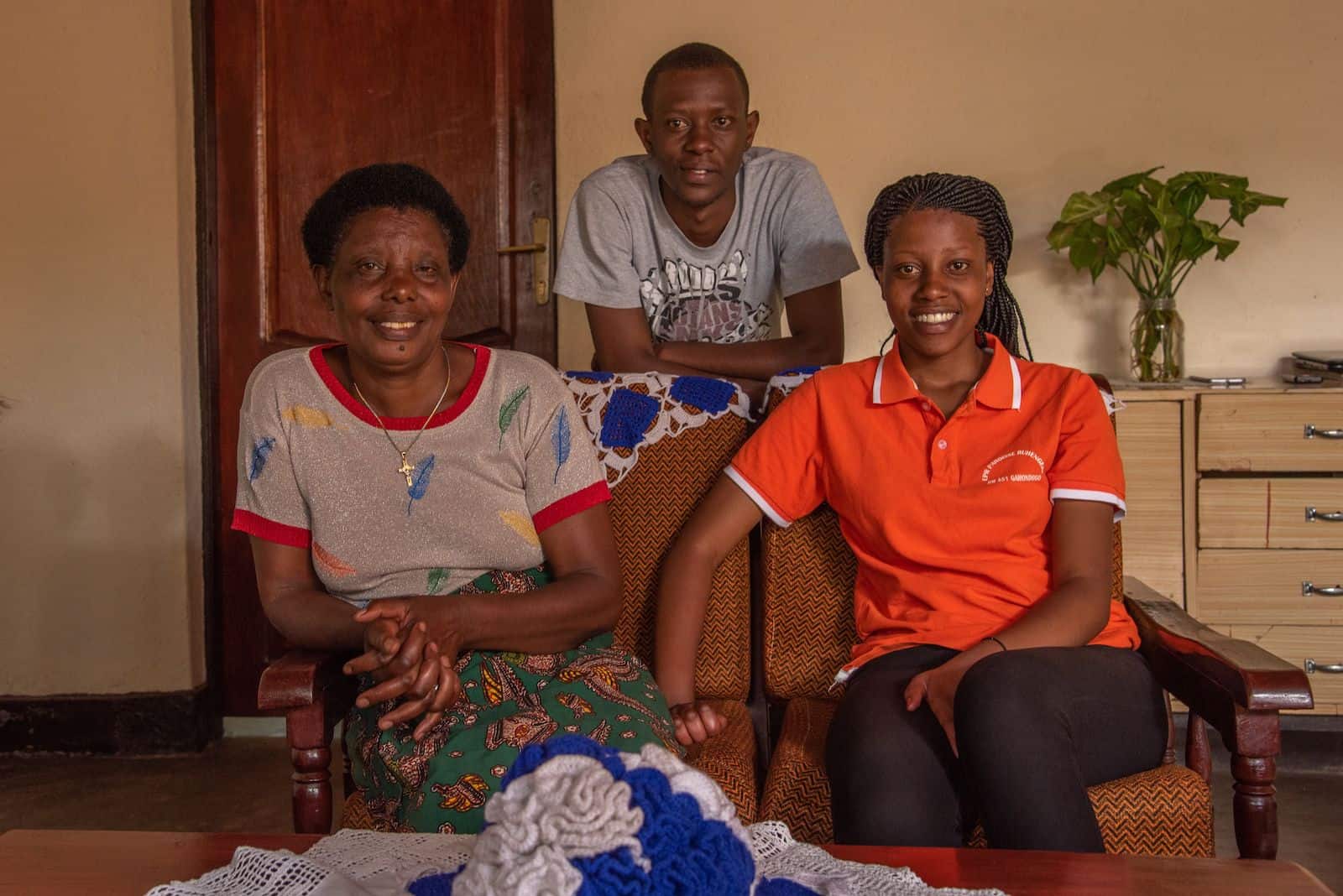 Two woman sit on a couch, with a young man standing behind them.