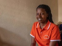 A young woman in an orange shirt smiles.
