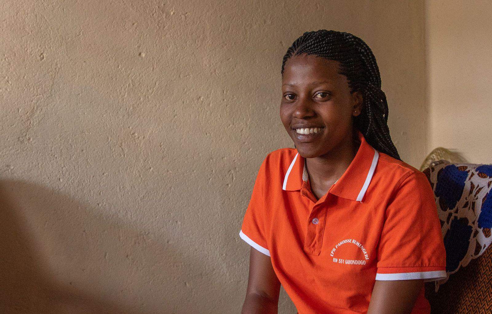 A young woman in an orange shirt smiles.