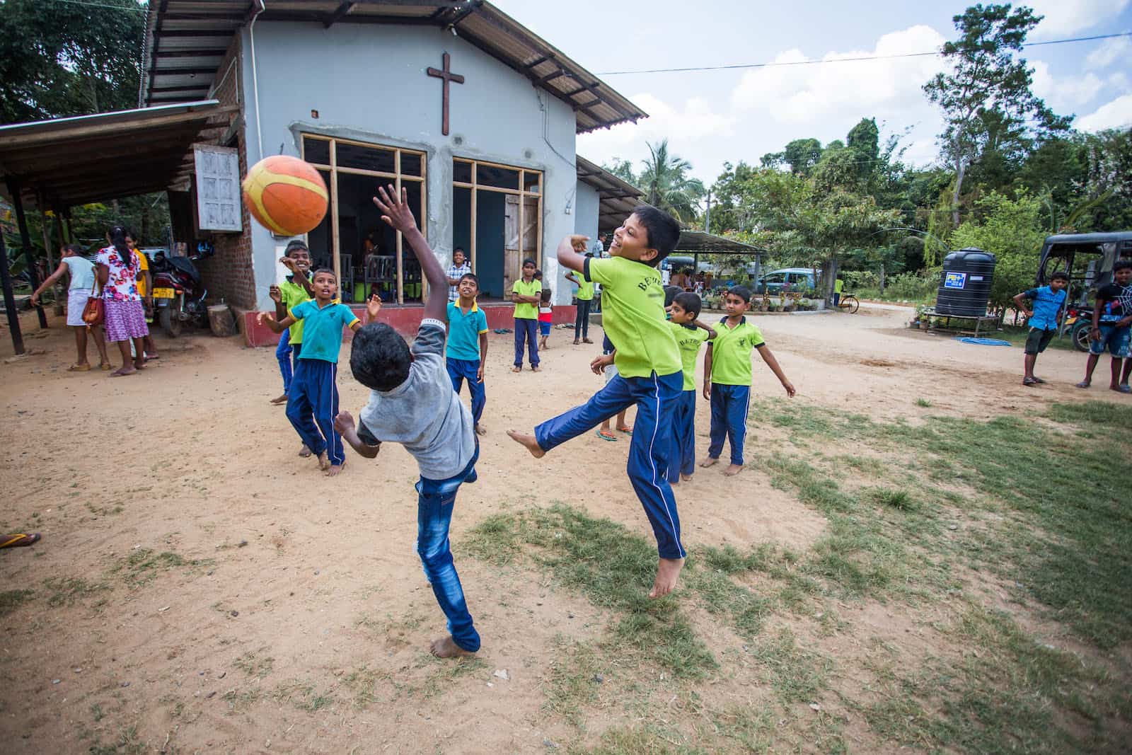 Boys jump for a basketball, playing outside of a church.