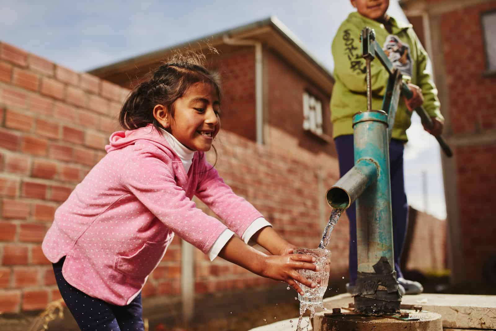 Kids Around the World: A girl gets water from a pump while a boy pumps.