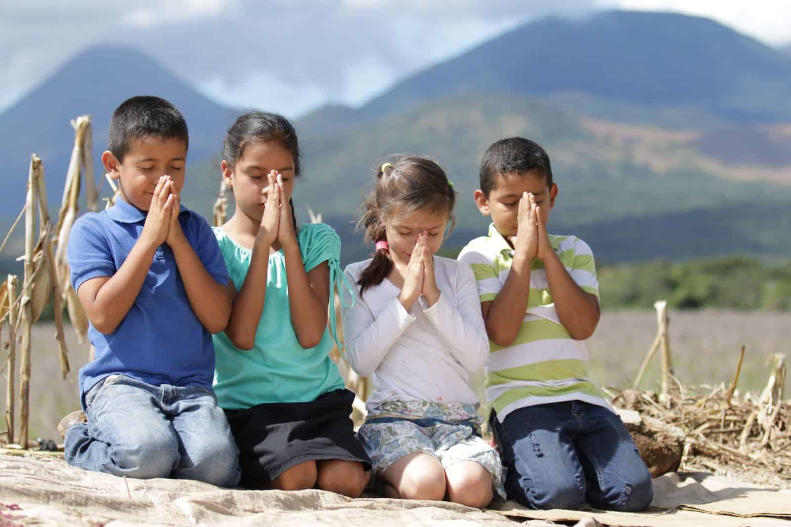 A group of four children sit outside, praying. 