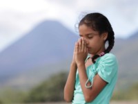 A girl in a green shirt prays, with her hands to her face.