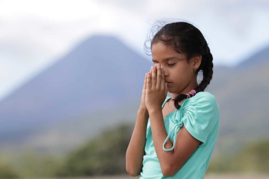 A girl in a green shirt prays, with her hands to her face.