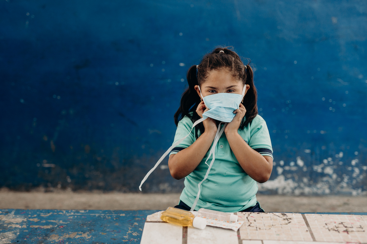 A girl wears a face mask, standing in front of a table with soap.