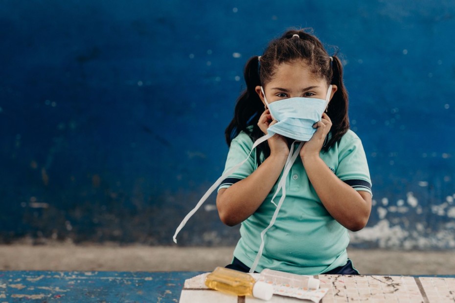 A girl wears a face mask, standing in front of a table with soap.