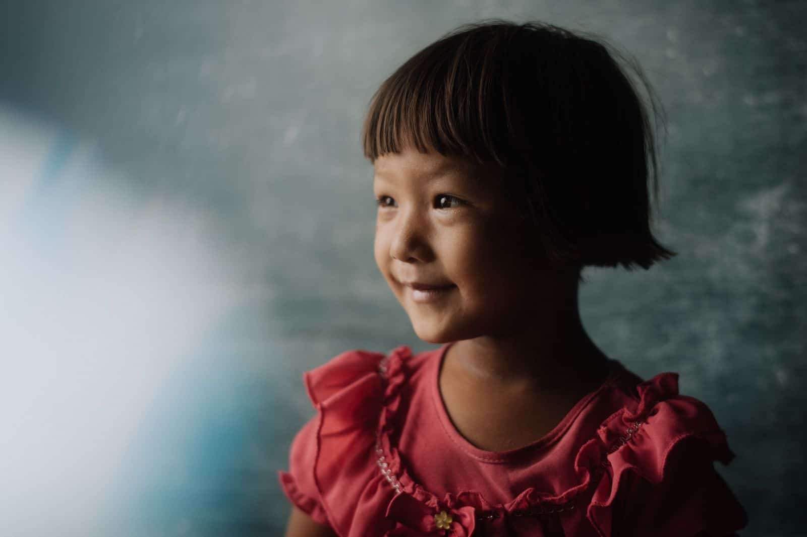 A girl in a pink dress looks to the side, smiling.