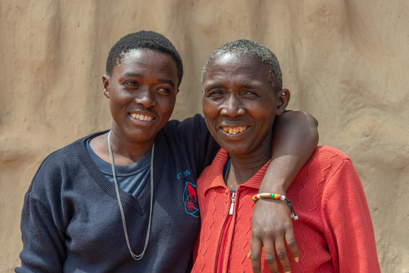 A young woman stands with her arm around a woman in red. 