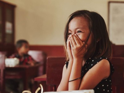 A girl laughs, face in her hands.