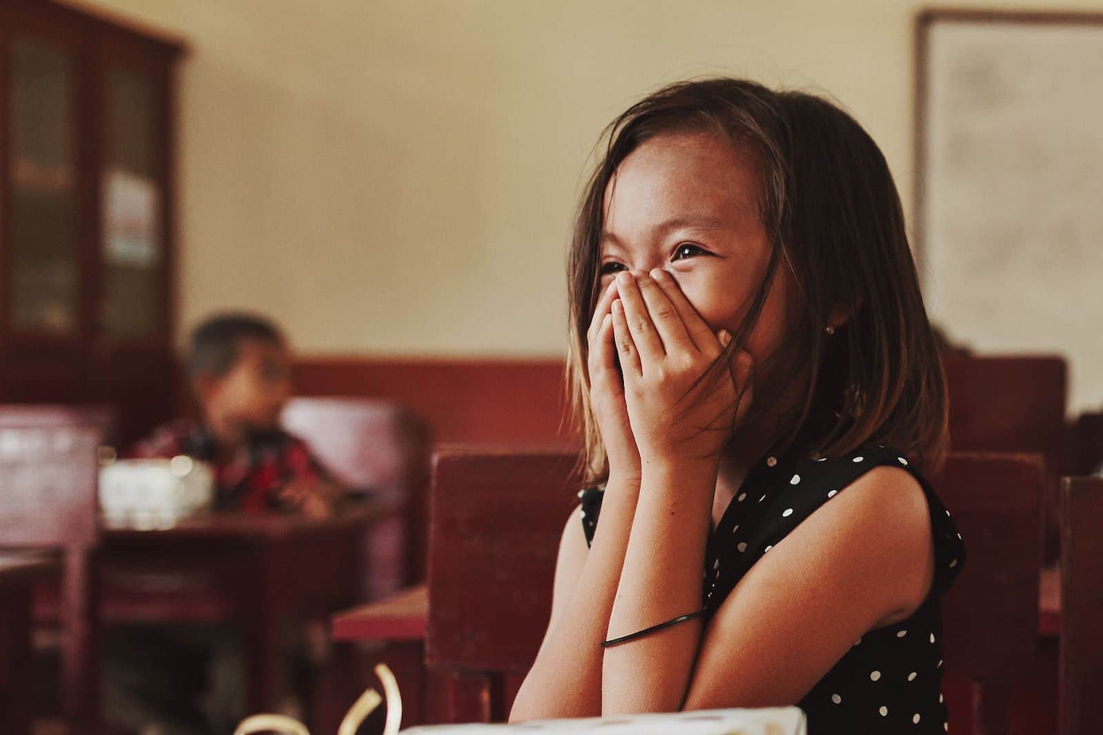 A girl laughs, face in her hands.