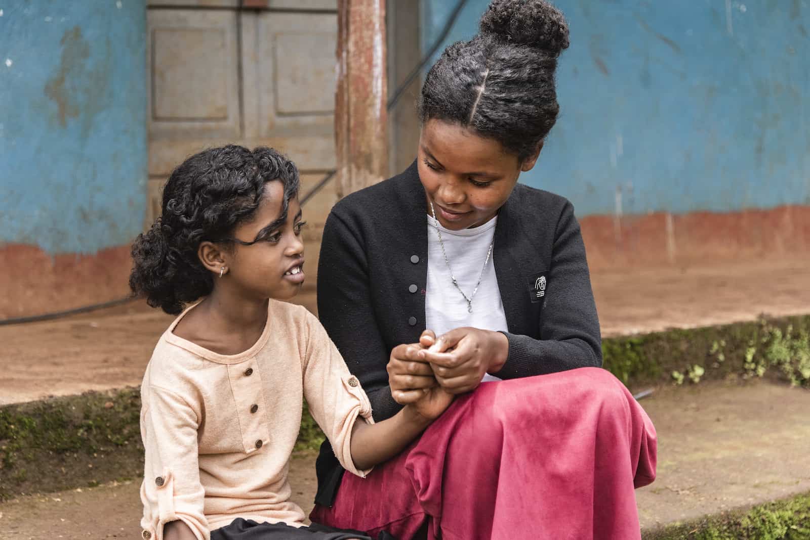 A young woman sits next to a girl, holding her hand and talking.