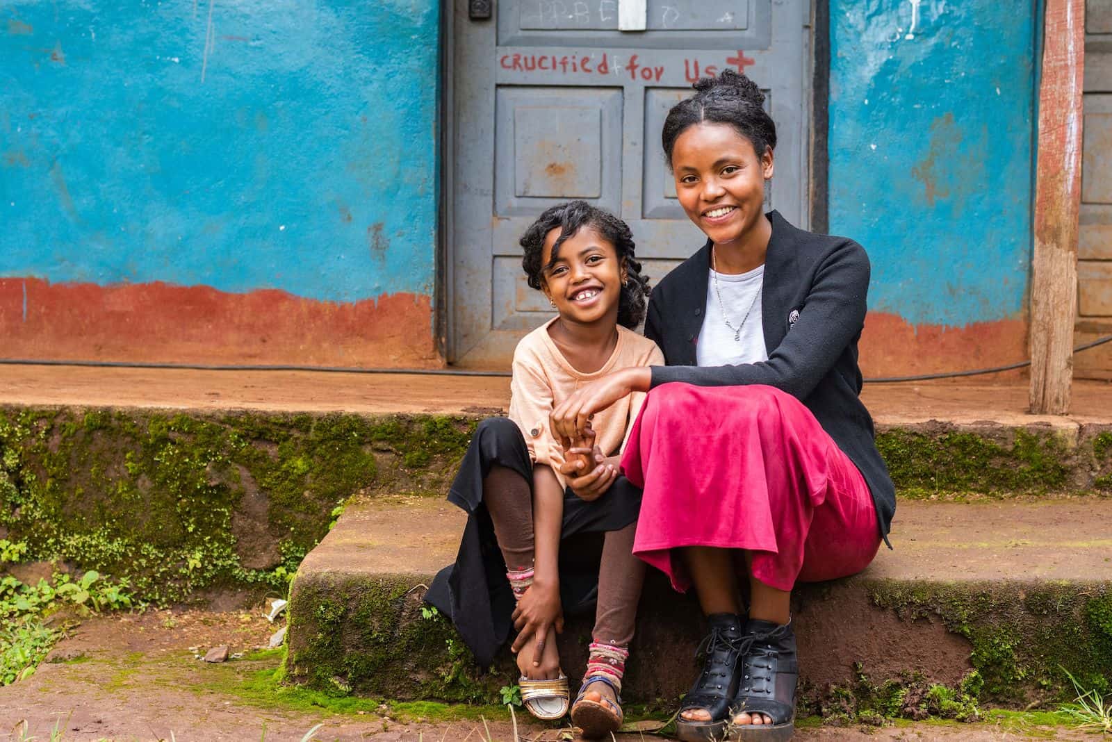A young woman and girl sit on a front step of a church.