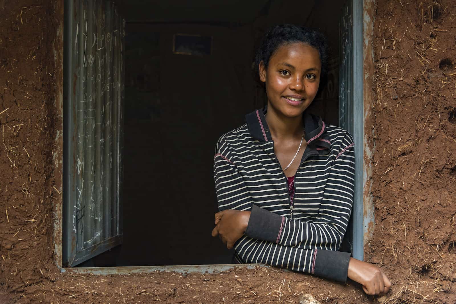 A woman stands in a window of a home made from adobe.