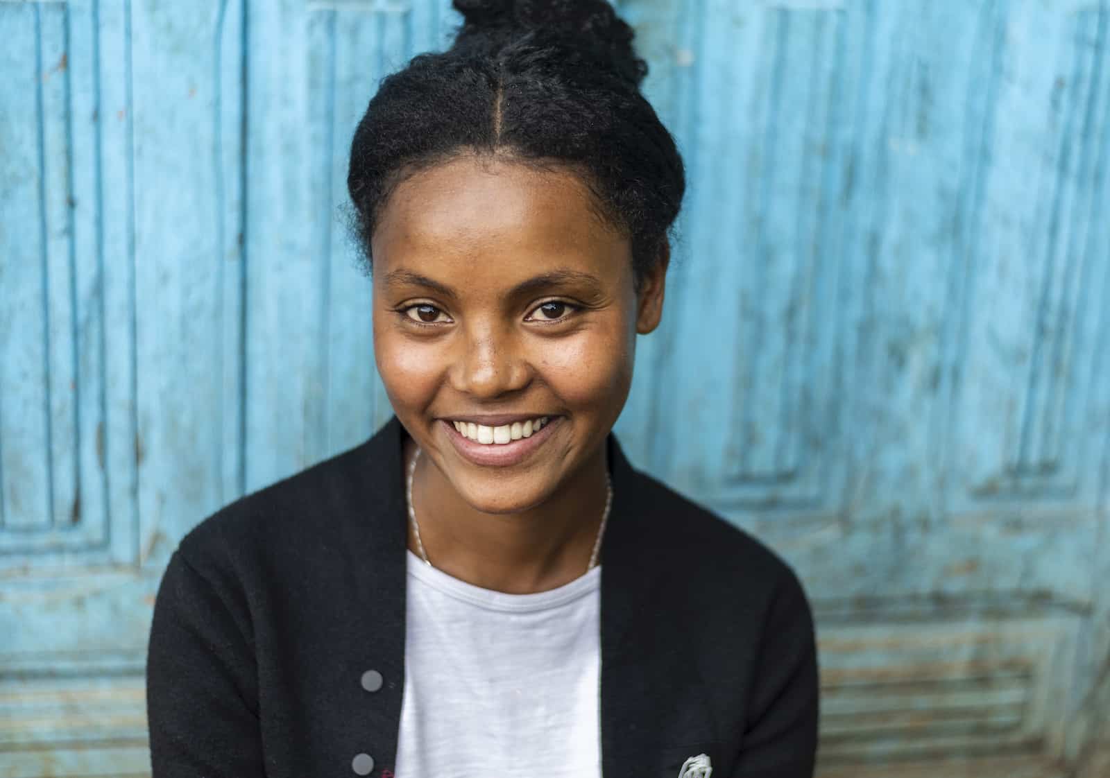 A young woman smiles, standing in front of a turquoise wall.