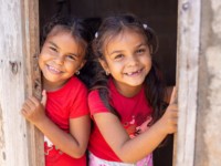 Two girls in red peek out of a door, smiling
