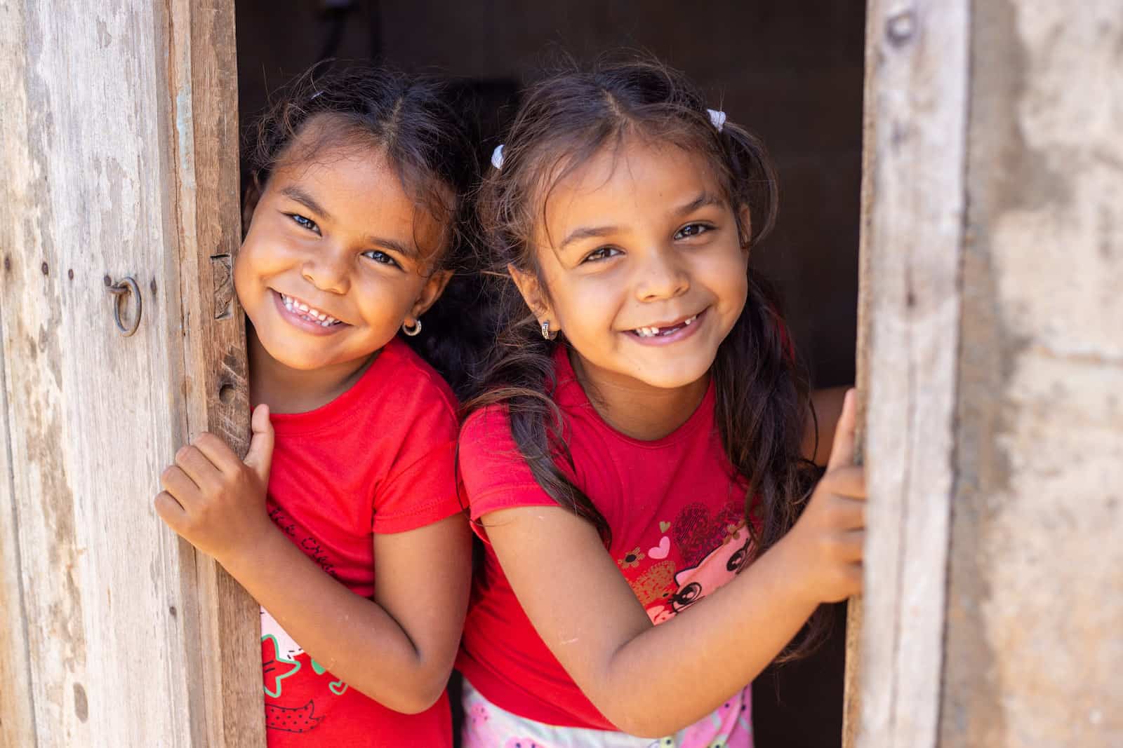 Two girls in red peek out of a door, smiling