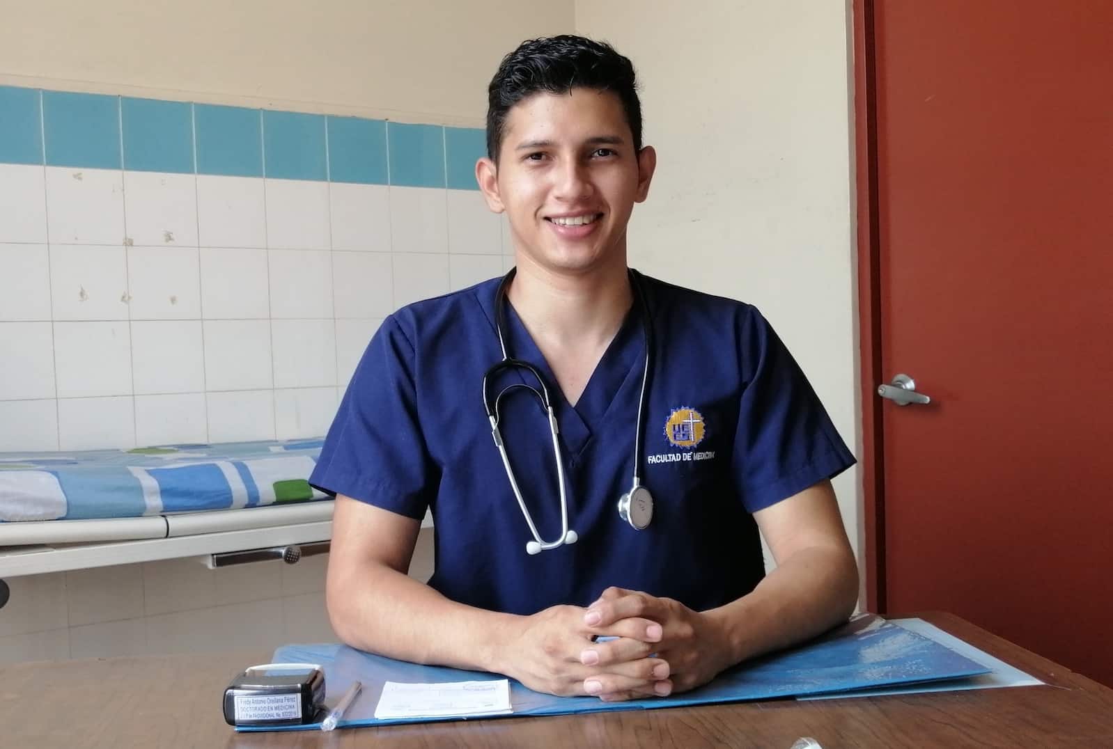 A man in scrubs with a stethoscope sits at a desk.