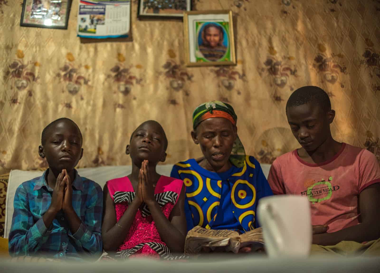 A woman reads the Bible while three children pray.