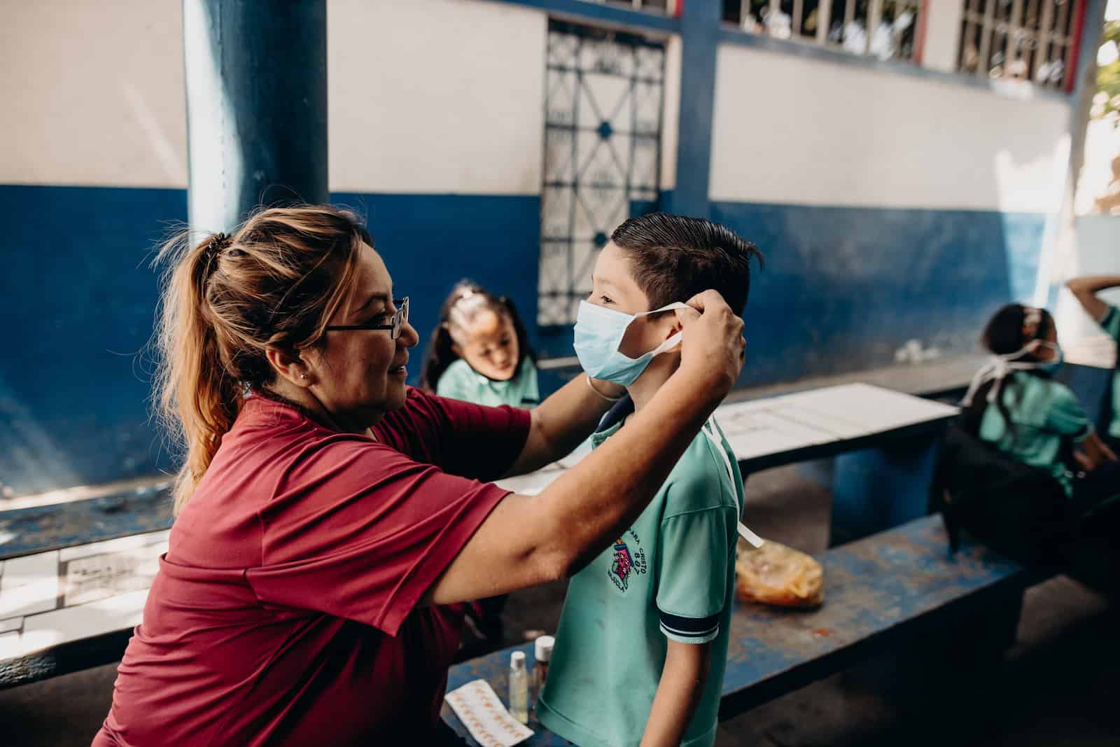 A woman secures a face mask on a boy.