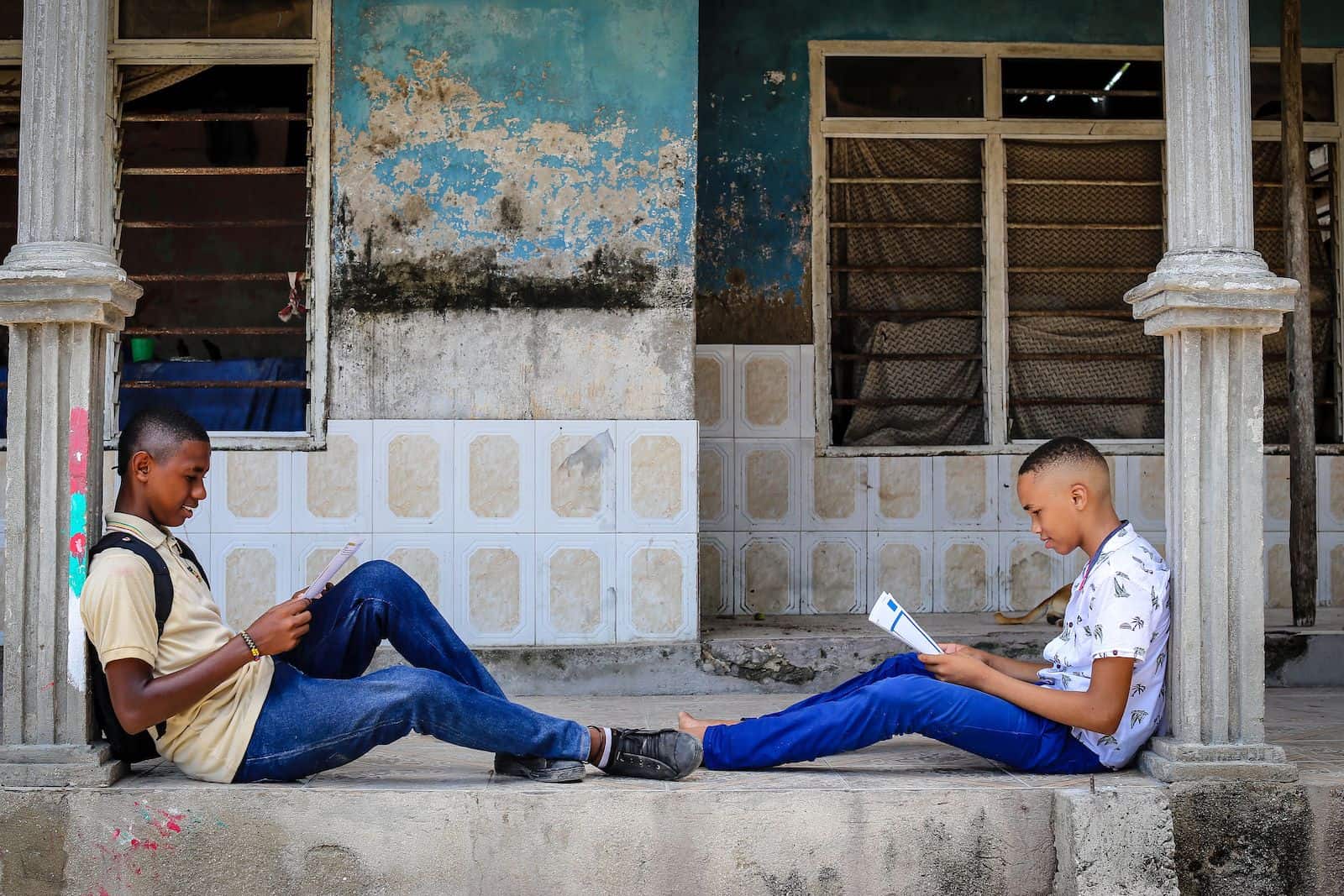 Two boys lean against columns, reading letters.