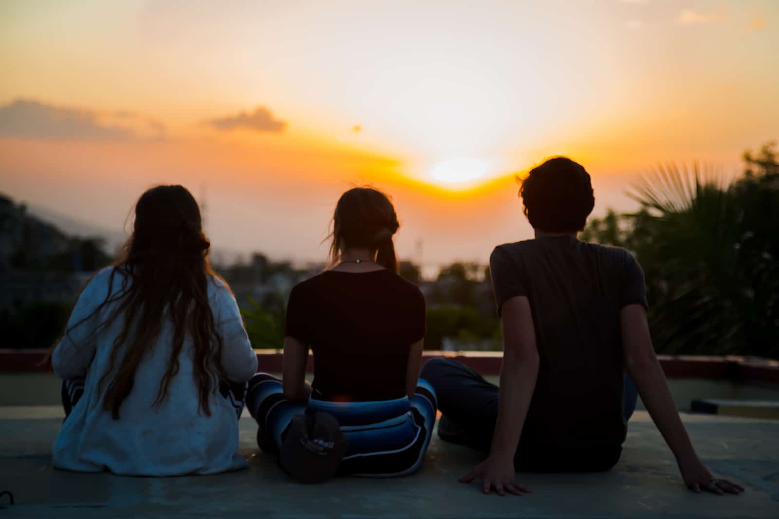 Three people sit cross-legged in front of a sunrise.