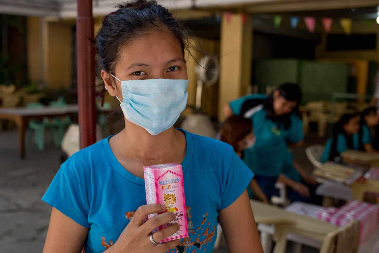 A young woman wearing a face mask holds a box of vitamins