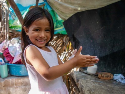 A girl in a pink dress washes her hands outside.