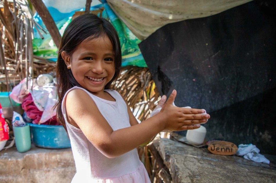 A girl in a pink dress washes her hands outside.