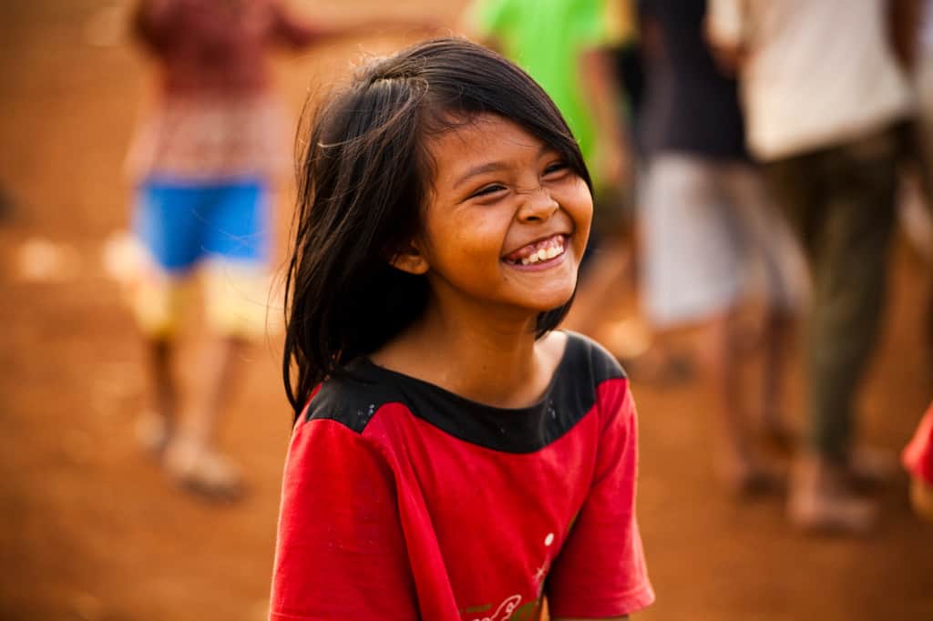 A little girl wearing a red shirt smiling so big her eyes are closed