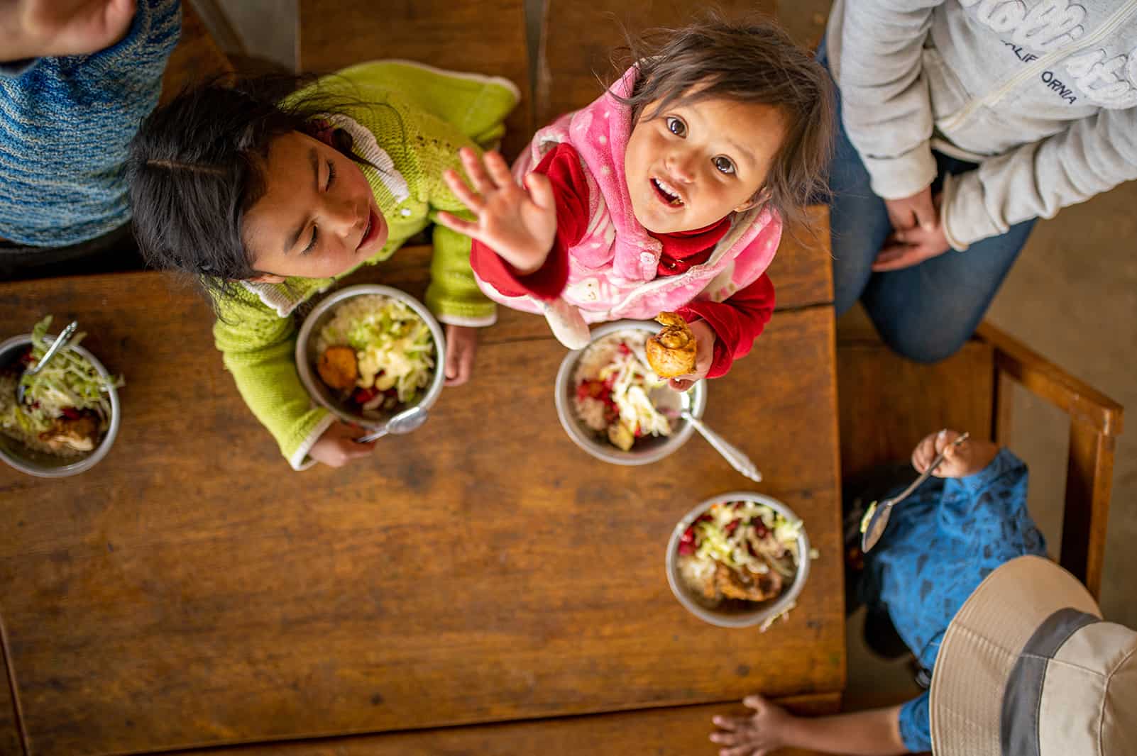 Children at a table eating looking at the camera above their heads