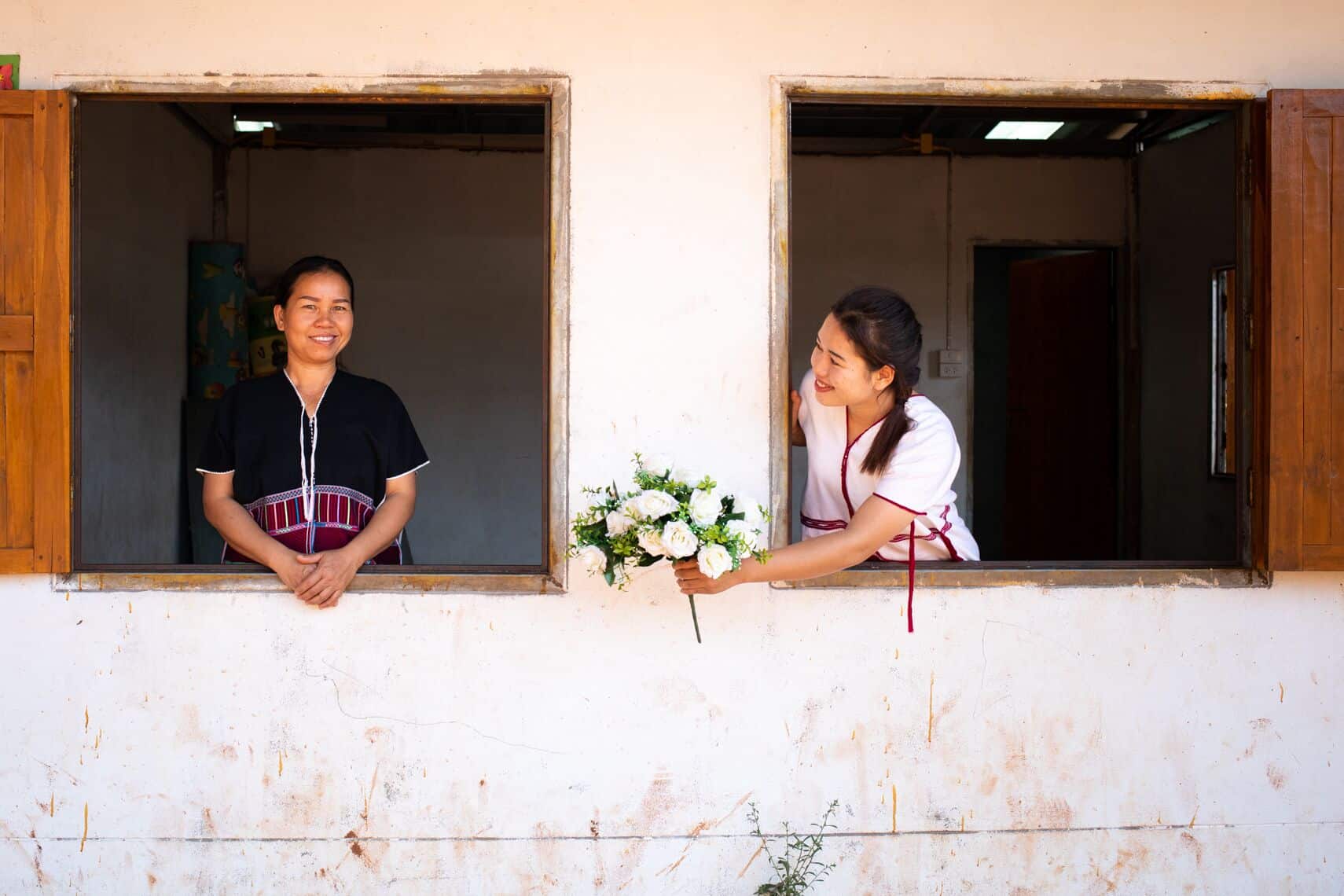 Daughter passing her mother flowers through a window