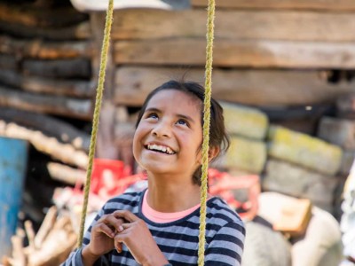 A girl sits on a swing, looking up and smiling.