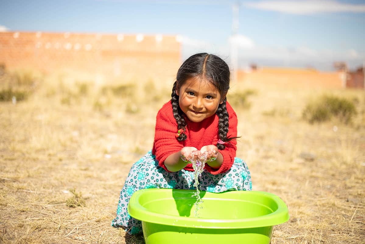 Happy girl washing her hands in a green bucket